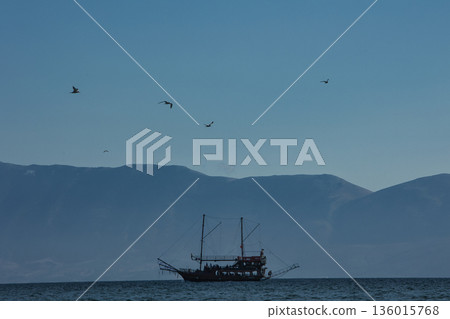 Vlore, Albania August 24 2025 A tourist pirate-style boat sails across the calm blue sea with distant mountains forming a soft silhouette on the horizon. 136015768