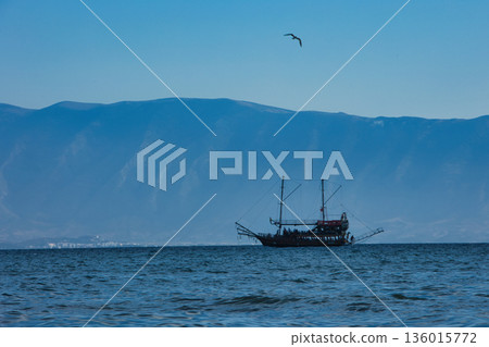 Vlore, Albania August 24 2025 A tourist pirate-style boat sails across the calm blue sea with distant mountains forming a soft silhouette on the horizon. Vlore, Albania August 24 2025 A tourist pirate-style boat sails across the calm blue sea with distant mountains forming a soft silhouette on the horizon. 136015772