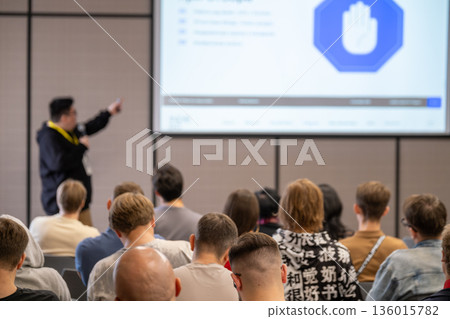 Presenter explains slides to attentive audience during conference seminar in modern lecture hall session live 136015782