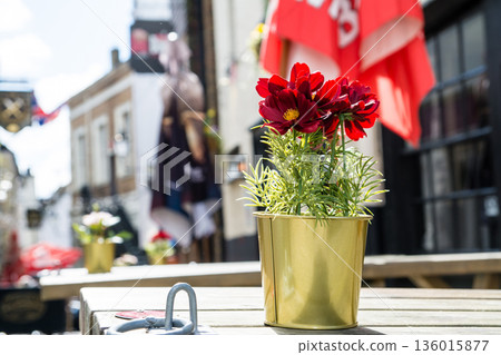 在倫敦郊區溫莎，一家商店前的桌子上擺放著一束鮮豔的紅花，沐浴在明媚的陽光下。 136015877