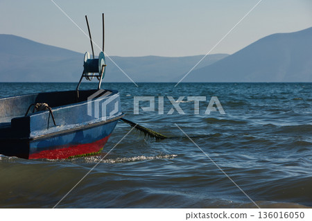 Silhouetted fishing boat on the shore of Vlora, Albania, captured on August 24, 2025. The backlit scene shows shimmering sunlight on the sea, gentle waves, and a swimmer in the background, creating a Silhouetted fishing boat on the shore of Vlora, Albania, captured on August 24, 2025. The backlit scene shows shimmering sunlight on the sea, gentle waves, and a swimmer in the background, creating a 136016050