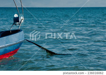 Silhouetted fishing boat on the shore of Vlora, Albania, captured on August 24, 2025. The backlit scene shows shimmering sunlight on the sea, gentle waves, and a swimmer in the background, creating a  136016062