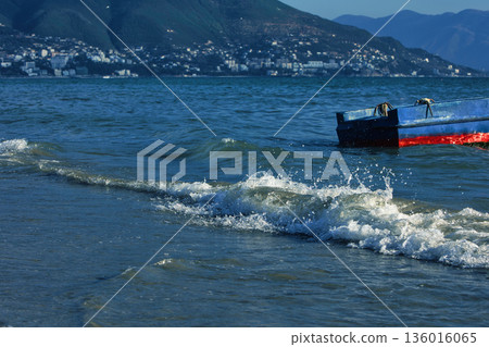 Silhouetted fishing boat on the shore of Vlora, Albania, captured on August 24, 2025. The backlit scene shows shimmering sunlight on the sea, gentle waves, and a swimmer in the background, creating a Silhouetted fishing boat on the shore of Vlora, Albania, captured on August 24, 2025. The backlit scene shows shimmering sunlight on the sea, gentle waves, and a swimmer in the background, creating a 136016065