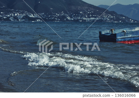 Silhouetted fishing boat on the shore of Vlora, Albania, captured on August 24, 2025. The backlit scene shows shimmering sunlight on the sea, gentle waves, and a swimmer in the background, creating a Silhouetted fishing boat on the shore of Vlora, Albania, captured on August 24, 2025. The backlit scene shows shimmering sunlight on the sea, gentle waves, and a swimmer in the background, creating a 136016066