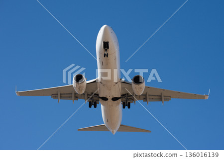 The plane lands. Airplane, passengers flying in the blue sky, preparing to land at the airport. View from below The plane lands. Airplane, passengers flying in the blue sky, preparing to land at the airport. View from below 136016139