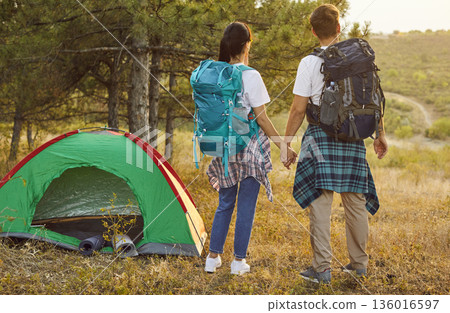 Back view of hikers couple by forest tent at golden sunset, weekend travel Back view of hikers couple by forest tent at golden sunset, weekend travel 136016597