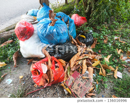 Pile of colorful garbage bags dumped on roadside causing environmental pollution Pile of colorful garbage bags dumped on roadside causing environmental pollution 136016996