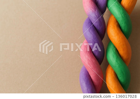 Intertwined colored bundles made of plasticine on a beige background. Space for text. 136017028