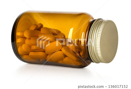 Amber glass bottle lying with orange pills 136017152