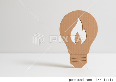 A cardboard light bulb with a flame cut out on a light background. Space for text. 136017414