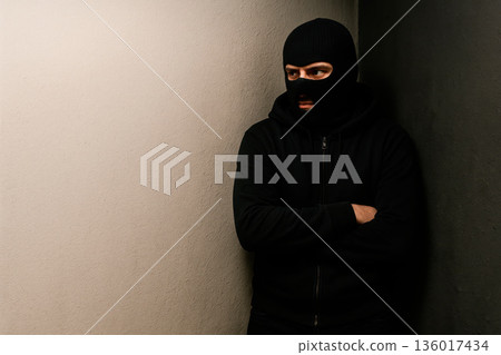 A criminal in a black mask hides in a corner. Space for text. A criminal in a black mask hides in a corner. Space for text. 136017434