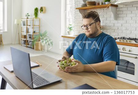 Plus-size man having diet salad at home kitchen during remote work time today 136017753