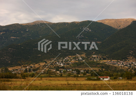 Hillside village landscape captured from the road in August 2025, showing traditional houses scattered across dry Mediterranean mountains under a calm summer sky. 136018138