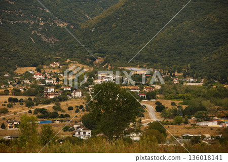 Hillside village landscape captured from the road in August 2025, showing traditional houses scattered across dry Mediterranean mountains under a calm summer sky. Hillside village landscape captured from the road in August 2025, showing traditional houses scattered across dry Mediterranean mountains under a calm summer sky. 136018141
