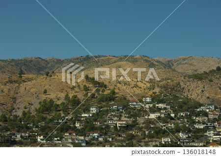 Hillside village landscape captured from the road in August 2025, showing traditional houses scattered across dry Mediterranean mountains under a calm summer sky. Hillside village landscape captured from the road in August 2025, showing traditional houses scattered across dry Mediterranean mountains under a calm summer sky. 136018148