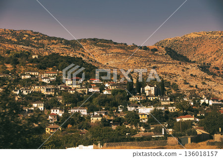 Hillside village landscape captured from the road in August 2025, showing traditional houses scattered across dry Mediterranean mountains under a calm summer sky. Hillside village landscape captured from the road in August 2025, showing traditional houses scattered across dry Mediterranean mountains under a calm summer sky. 136018157
