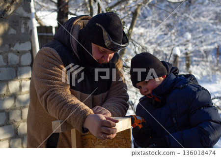 A father and son spend time together on a winter day, working on a DIY woodworking project outdoors and using tools to assemble a wooden structure. 136018474