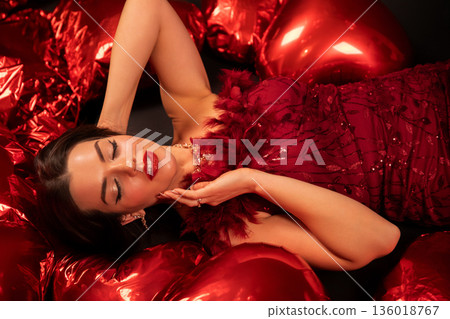 Woman relaxes among red heart-shaped pillows on Valentines Day in a cozy setting while wearing a stunning dress Woman relaxes among red heart-shaped pillows on Valentines Day in a cozy setting while wearing a stunning dress 136018767