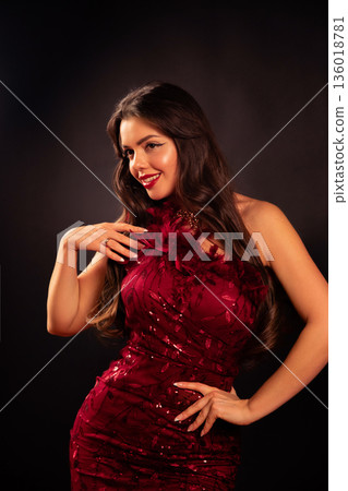 Woman in a red dress posing with a smile for Valentines Day celebration indoors at night Woman in a red dress posing with a smile for Valentines Day celebration indoors at night 136018781