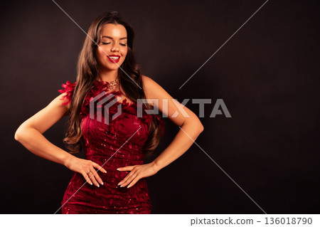 Woman poses confidently in red dress for Valentines Day celebration with a bright smile in a studio setting 136018790