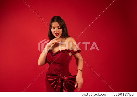 Woman in red dress shows beauty and love for Valentines Day celebration in a studio setting with a red background Woman in red dress shows beauty and love for Valentines Day celebration in a studio setting with a red background 136018796