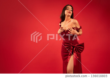 Woman in red dress poses confidently in front of red backdrop for Valentines Day celebration 136018803