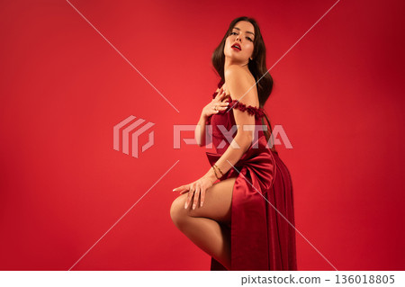 Woman poses with confidence wearing a red dress during Valentine celebration in a studio Woman poses with confidence wearing a red dress during Valentine celebration in a studio 136018805