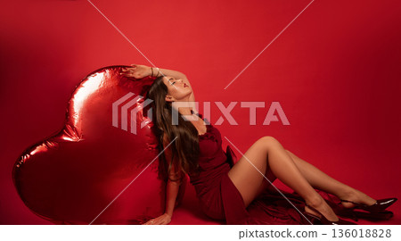 Woman poses in red dress next to heart-shaped balloon for Valentines Day celebration 136018828