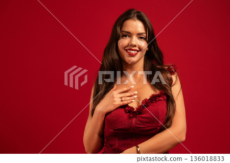 Beautiful woman smiles and shows love for Valentines Day with red background and elegant outfit 136018833