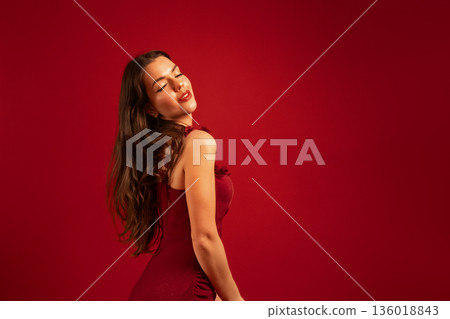 Beautiful woman poses in red dress against a red background for Valentines Day celebration Beautiful woman poses in red dress against a red background for Valentines Day celebration 136018843