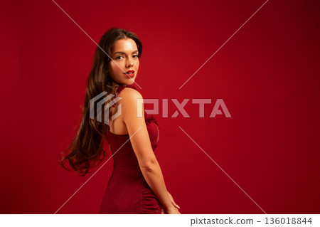 Woman poses in a red dress against a red backdrop for Valentines Day celebration in a studio setting Woman poses in a red dress against a red backdrop for Valentines Day celebration in a studio setting 136018844