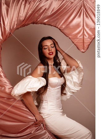 Beautiful woman in a white dress posing with pink fabric on Valentines Day setting in a studio 136018849
