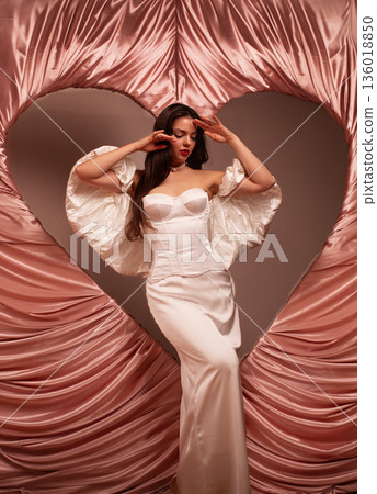 Beautiful woman poses in a white dress with heart backdrop for Valentines Day celebration Beautiful woman poses in a white dress with heart backdrop for Valentines Day celebration 136018850