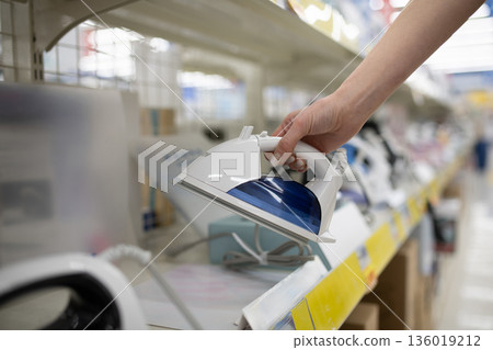 一位女士的手正在家電商店挑選熨斗。 一位女士的手正在家電商店挑選熨斗。 136019212