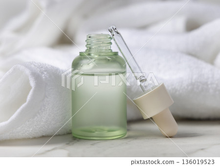 Pipette next to opened green glass dropper bottle near white bath towel, cosmetic mockup 136019523