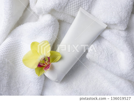 Mockup of white blank squeeze cosmetic tube with yellow orchid flower on bath towel 136019527