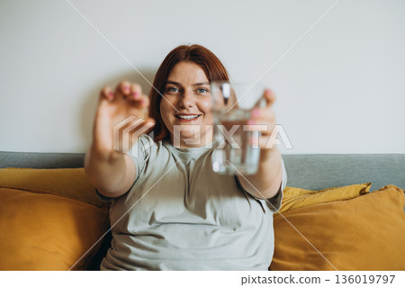 Dietary supplement, healthy diet positive young woman hand holding pill capsule, take vitamin in mouth for beauty skin hair, taking medicine with glass of water at home, pharmacy and health care 136019797