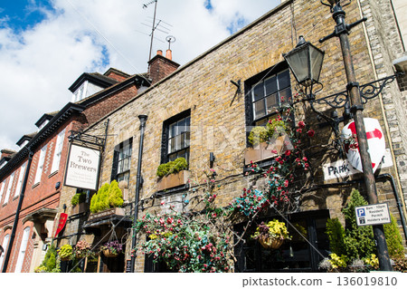 A historic brick building decorated with a pub sign and plants in bright sunlight in Windsor, a suburb of London 136019810