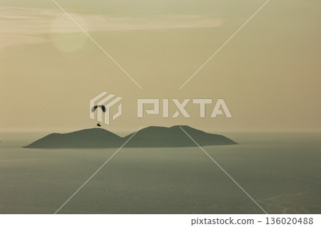 Mountain range rising above a calm blue sea under a clear sky, forming a minimalistic coastal landscape. Serene natural scenery captured on August  2025. 136020488