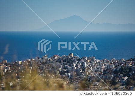 Mountain range rising above a calm blue sea under a clear sky, forming a minimalistic coastal landscape. Serene natural scenery captured on August  2025. 136020500