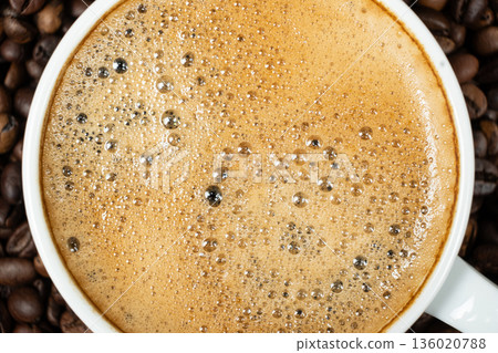 Top view of a white cup filled with fresh espresso on a coffee bean background. Top view of a white cup filled with fresh espresso on a coffee bean background. 136020788