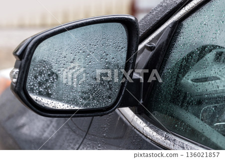 A detailed close-up of a wet car side mirror and window 136021857