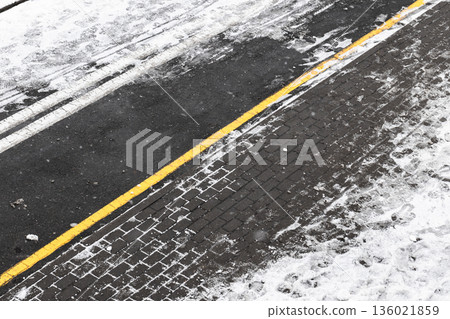 A snowy urban street edge shows a bright yellow line and snowy asphalt 136021859