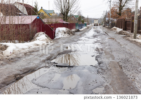 A muddy, puddled rural street lined with fences, bare trees and snow piles A muddy, puddled rural street lined with fences, bare trees and snow piles 136021873