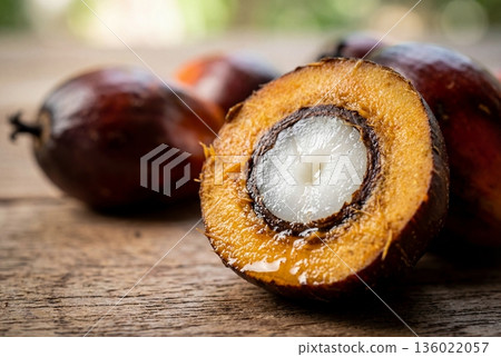 Halved oil palm fruit with visible white kernel and fibrous orange mesocarp on wood 136022057