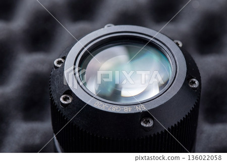 Close up view of black industrial proximity sensor with glass lens and screws on dark foam background 136022058