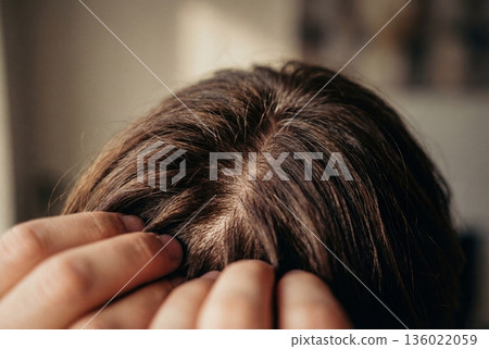 Close up view of dark brown hair being parted by fingers to inspect the scalp and roots 136022059