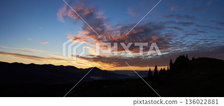 Breathtaking sunset paints sky with vibrant hues of pink, orange, purple, blending into blue morning sky. Silhouetted mountains, pine trees create serene backdrop. Tranquil and picturesque landscape. Breathtaking sunset paints sky with vibrant hues of pink, orange, purple, blending into blue morning sky. Silhouetted mountains, pine trees create serene backdrop. Tranquil and picturesque landscape. 136022881