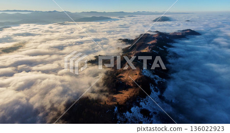 Breathtaking aerial view of mountain ridge piercing through sea of clouds. Sunlight illuminates patches of ridge. Distant mountain ranges create serene and expansive horizon. Breathtaking aerial view of mountain ridge piercing through sea of clouds. Sunlight illuminates patches of ridge. Distant mountain ranges create serene and expansive horizon. 136022923