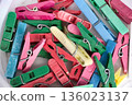 The background is made of multi-colored clothespins for hanging washed clothes, they lie in a white container. 136023137